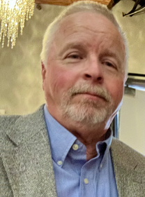 Koontz - Wisconsin Dairy Products Associa Portrait of an older man with light hair and a goatee, wearing a blue shirt and gray blazer indoors, looking at the camera with a neutral expression.